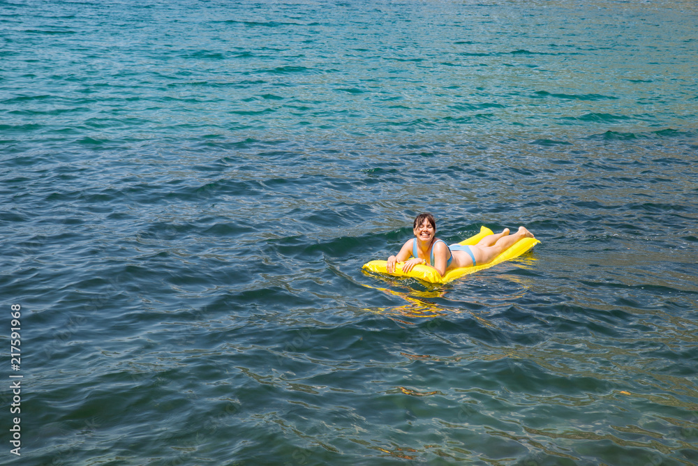 young adult woman on yellow mattress in blue sea water.