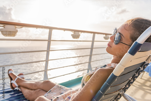 Cruise ship vacation woman relaxing lying on deck lounger at sunset casual lifestyle. Girl enjoying sunshine laid back sleeping on balcony chair on travel summer holidays.