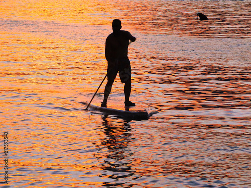 Man on a paddle board against the sea during sunset