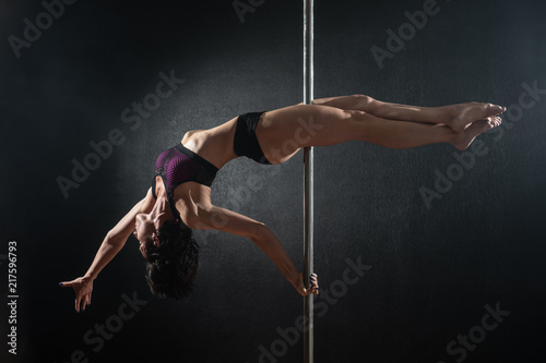 Beautiful slim girl with pylon. Female pole dancer dancing on a black background