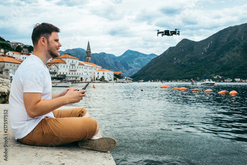 man control drone while sitting at pier in old european city. beautiful view of sea and mountains on background