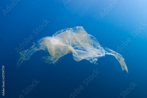 A shredded, discarded plastic bag floating underwater in a tropical ocean creating a hazard to marine life