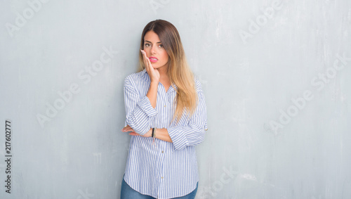Young adult woman over grey grunge wall wearing fashion business outfit thinking looking tired and bored with depression problems with crossed arms. © Krakenimages.com