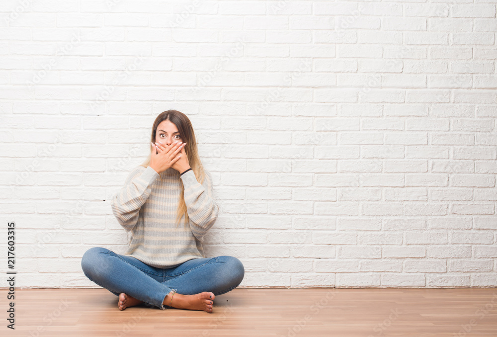 Young adult woman sitting on the floor over white brick wall at home shocked covering mouth with hands for mistake. Secret concept. Young adult woman sitting on the floor over white brick wall at home shocked covering mouth with hands for mistake. Secret concept.