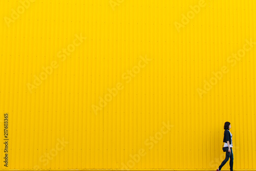 Woman walking near yellow wall, copy space background