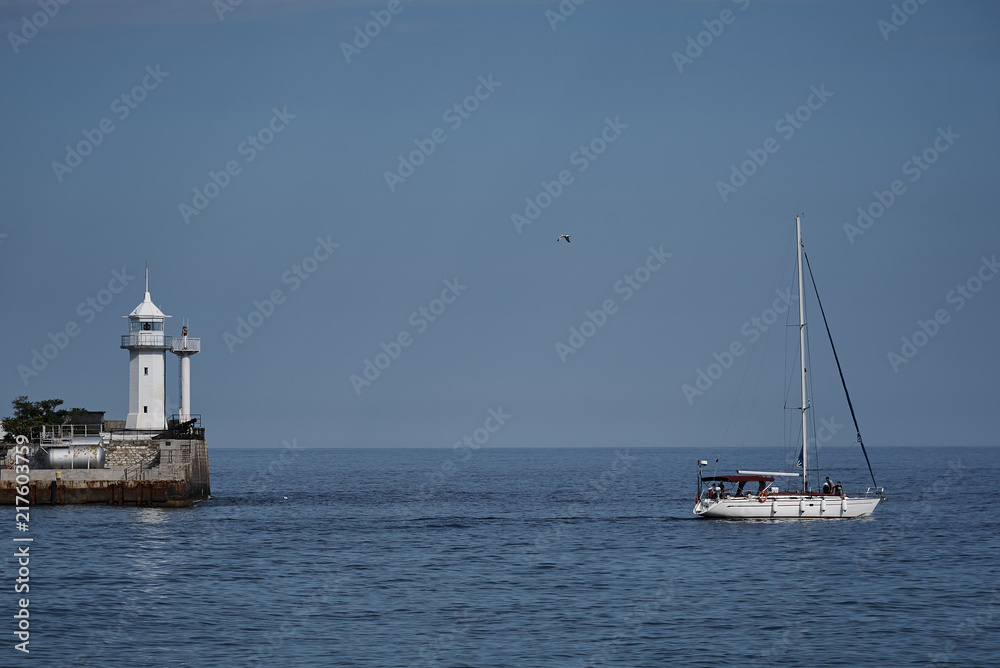 View of the lighthouse in the sea and a floating white yacht.