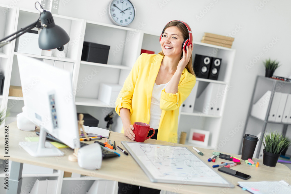 A young girl in headphones stands near a table with a red mug in her hands. Before the girl on the table is a magnetic board