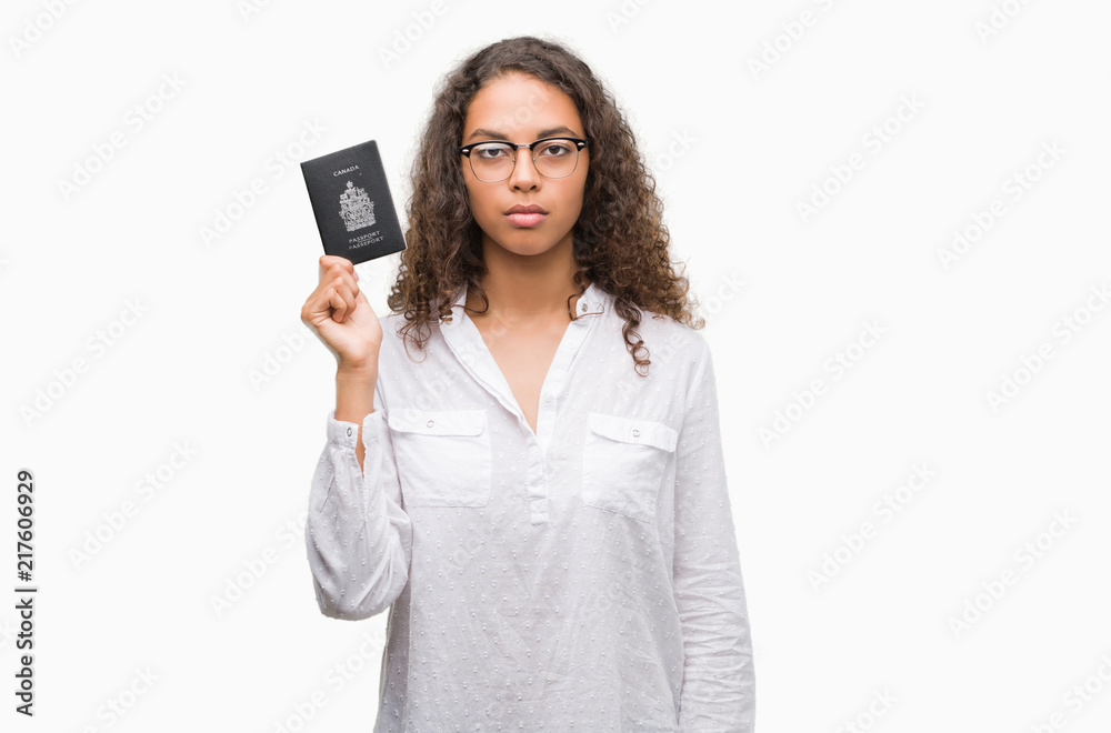 Young hispanic woman holding passport of Canada with a confident expression on smart face thinking serious Young hispanic woman holding passport of Canada with a confident expression on smart face thinking serious