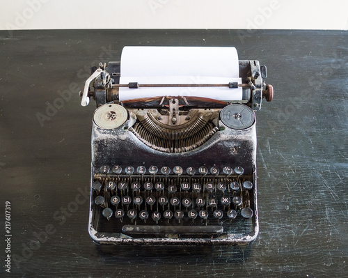 An old typewriter on an old black table with a sheet of paper.