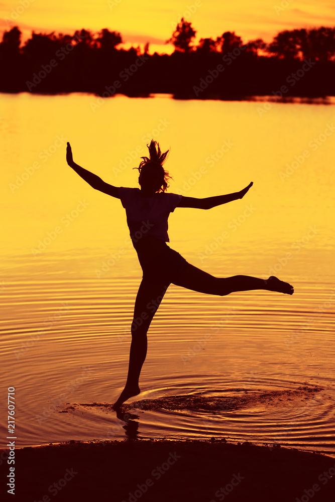 Cheerful athletic girl practicing for the beautiful red sunset background. 