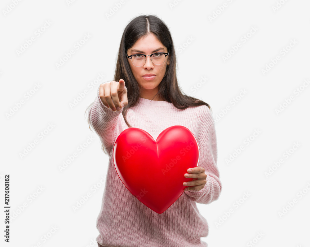 Young hispanic woman holding heart in love pointing with finger to the camera and to you, hand sign, positive and confident gesture from the front Young hispanic woman holding heart in love pointing with finger to the camera and to you, hand sign, positive and confident gesture from the front