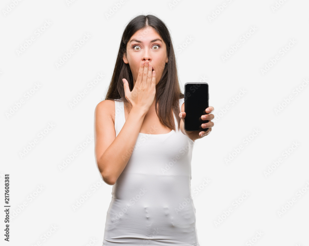 Young beautiful hispanic showing smartphone cover mouth with hand shocked with shame for mistake, expression of fear, scared in silence, secret concept Young beautiful hispanic showing smartphone cover mouth with hand shocked with shame for mistake, expression of fear, scared in silence, secret concept