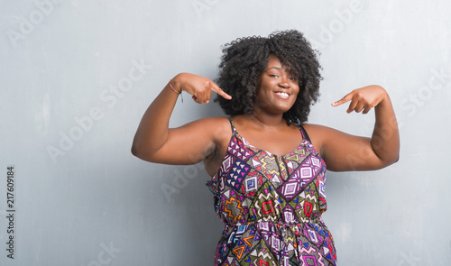 Young african american woman over grey grunge wall wearing colorful dress looking confident with smile on face, pointing oneself with fingers proud and happy. photo