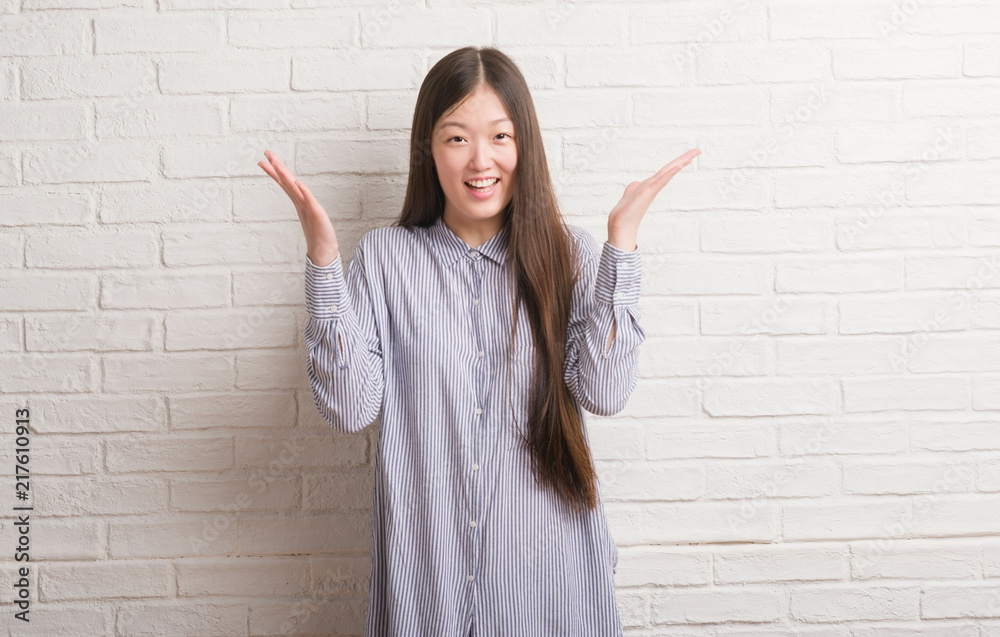 Young Chinese woman over brick wall very happy and excited, winner expression celebrating victory screaming with big smile and raised hands Young Chinese woman over brick wall very happy and excited, winner expression celebrating victory screaming with big smile and raised hands