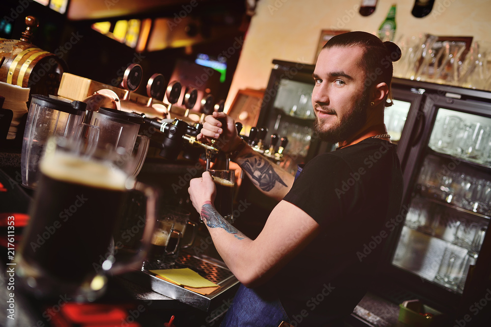 young attractive man bartender pours beer into mug and looks into camera
