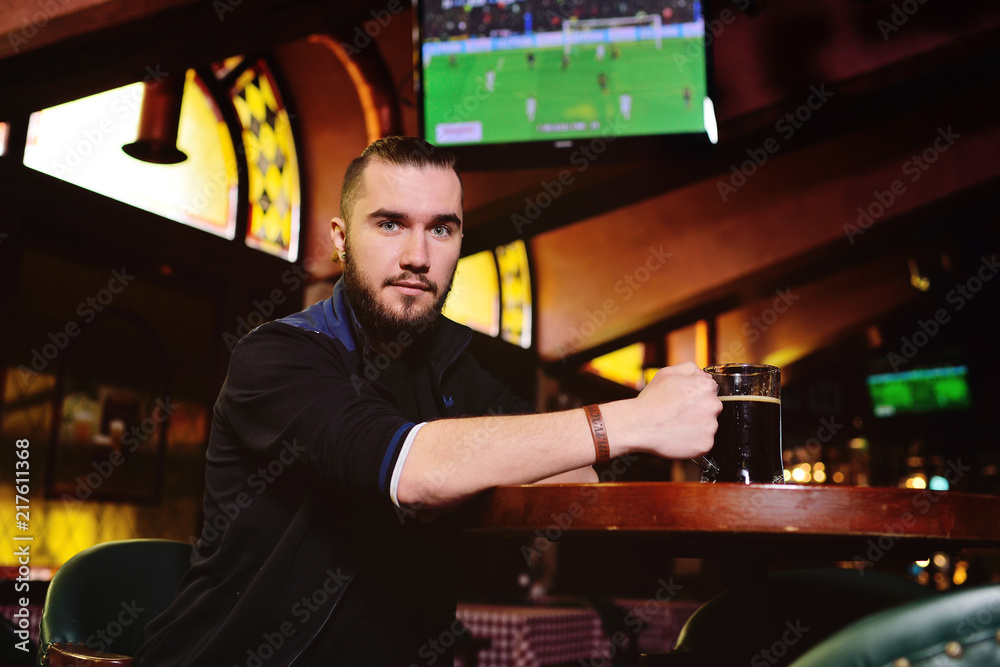 young attractive bearded man drinking beer in pub and watching football