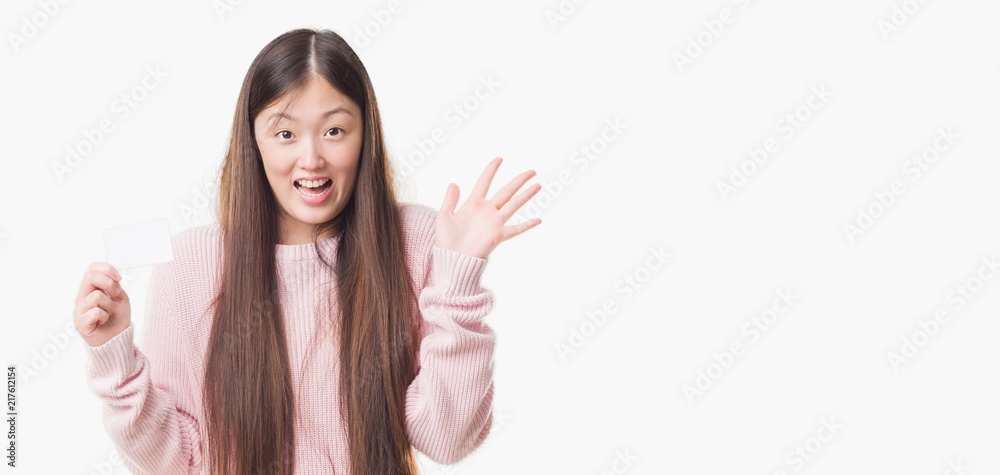 Young Chinese woman over isolated background holding visit card very happy and excited, winner expression celebrating victory screaming with big smile and raised hands Young Chinese woman over isolated background holding visit card very happy and excited, winner expression celebrating victory screaming with big smile and raised hands