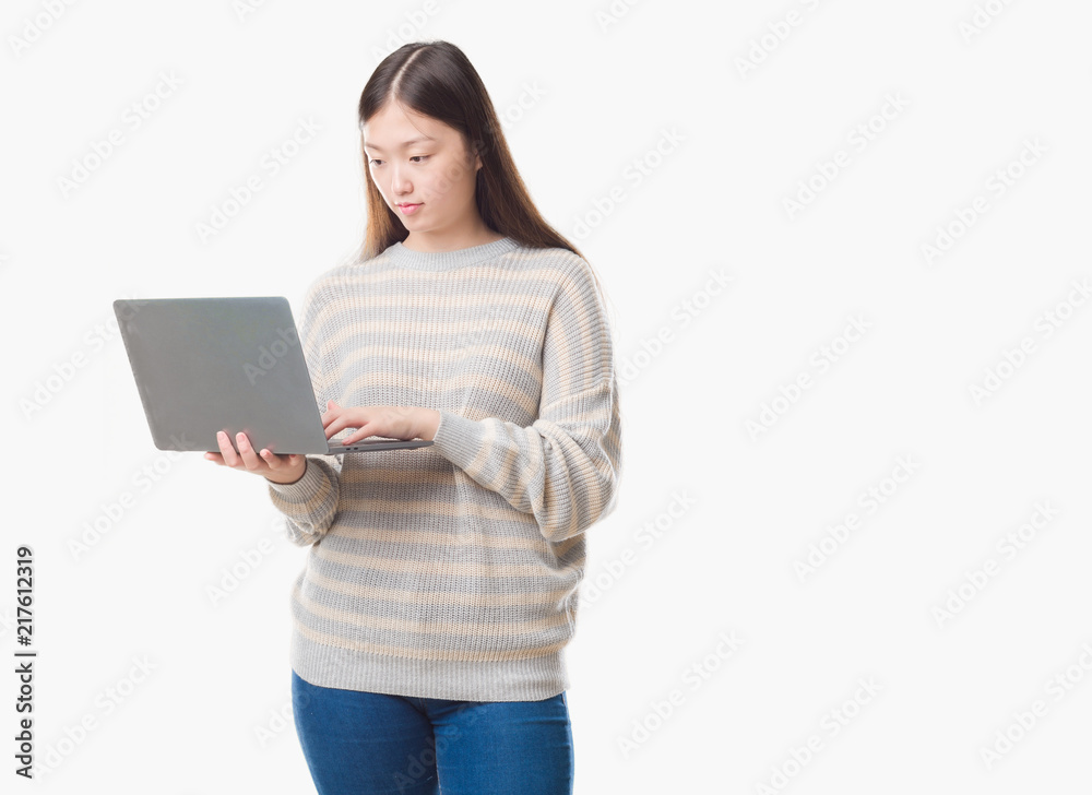 Naklejka premium Young Chinese woman over isolated background using computer laptop with a confident expression on smart face thinking serious