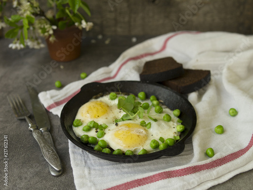 Delicious breakfast - fried eggs with green peas. On a dark background. Close up, copy space