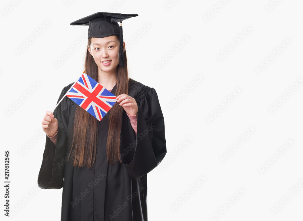 Young Chinese woman wearing graduate uniform holding United kingdom flag with a happy face standing and smiling with a confident smile showing teeth