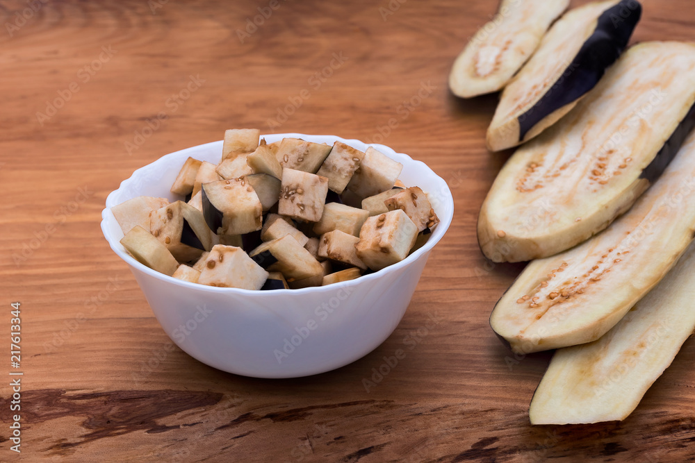 Eggplant cut into longitudinal slices and finely diced in a plate on a wooden background. Eggplant cut into longitudinal slices and finely diced in a plate on a wooden background.