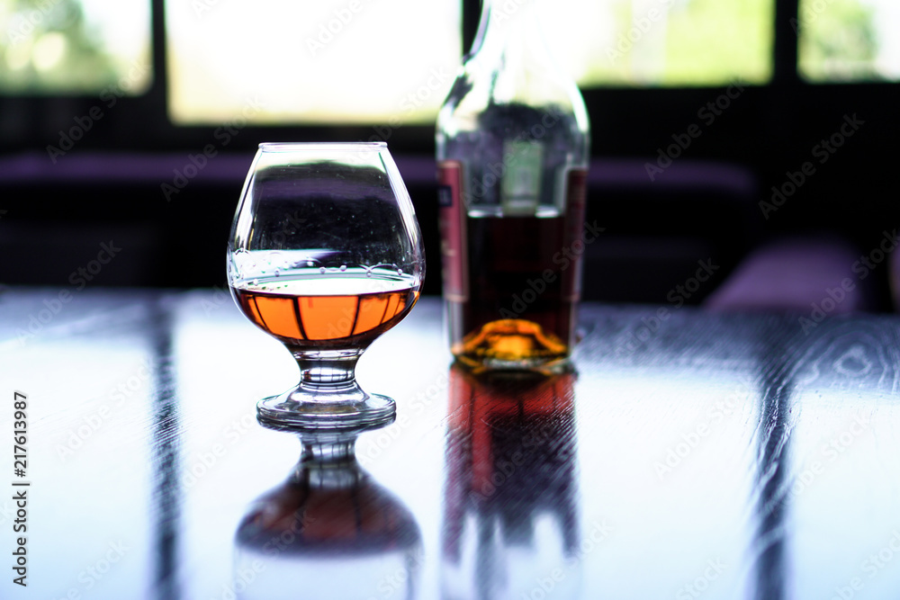 A glass of cognac on a black table with a bottle of cognac in the background. A glass of cognac on a black table with a bottle of cognac in the background.