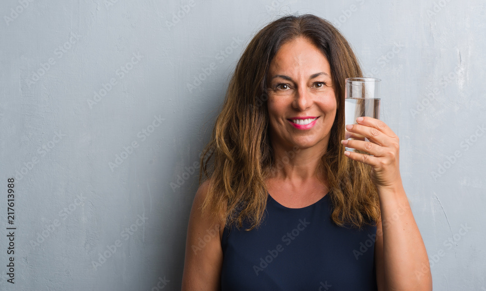 Middle age hispanic woman drinking glass of water with a happy face standing and smiling with a confident smile showing teeth Middle age hispanic woman drinking glass of water with a happy face standing and smiling with a confident smile showing teeth