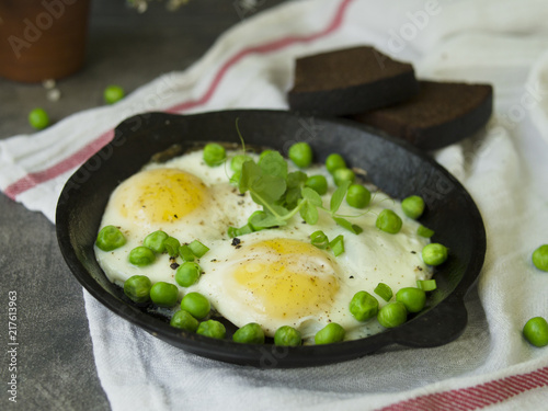 Delicious breakfast - fried eggs with green peas. On a dark background. Close up, copy space, top view, flat lay