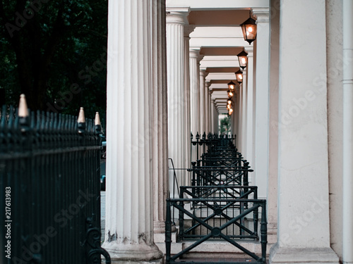 Diminishing perspective view of tall white columns, black iron cast fences, and antique lanterns of Victorian townhouses in London.
