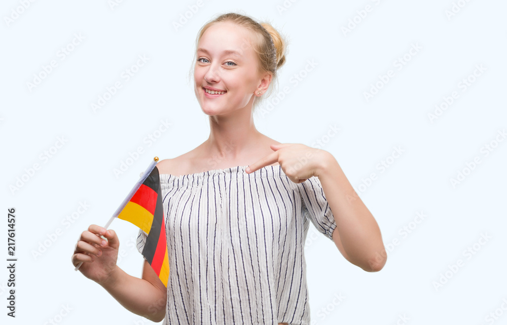 Blonde teenager woman holding flag of Germany with surprise face pointing finger to himself Blonde teenager woman holding flag of Germany with surprise face pointing finger to himself