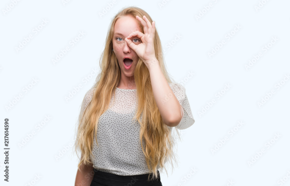 Blonde teenager woman wearing moles shirt doing ok gesture shocked with surprised face, eye looking through fingers. Unbelieving expression. Blonde teenager woman wearing moles shirt doing ok gesture shocked with surprised face, eye looking through fingers. Unbelieving expression.
