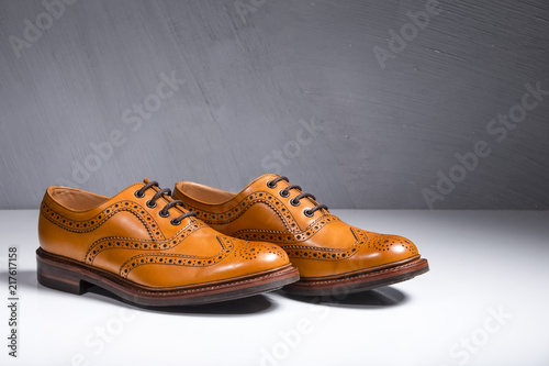 Closeup of Pair of Luxury Male Full Broggued Tan Leather Oxfords Shoes On White Surface. Against Gray Wall.