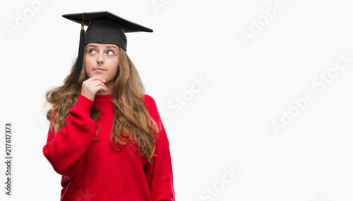 Young blonde woman wearing graduation cap serious face thinking about question, very confused idea