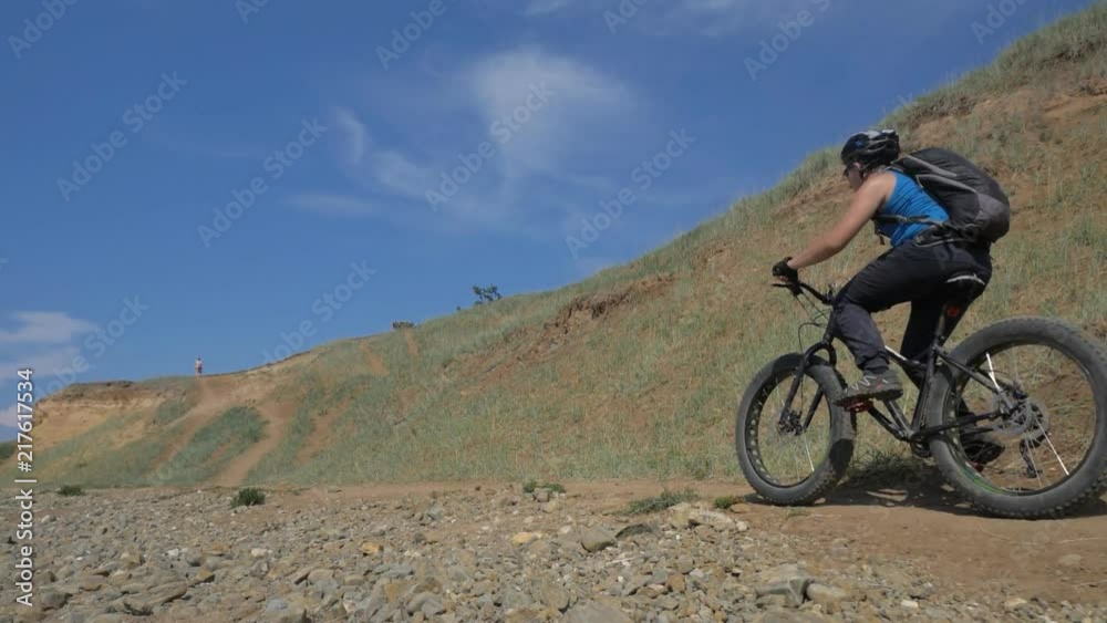 Fat bike also called fatbike or fat-tire bike in summer driving on the road. The guy rides by the hill on a sand clay path, behind him the shore by the sea. Slow motion shooting 180fps. Fat bike also called fatbike or fat-tire bike in summer driving on the road. The guy rides by the hill on a sand clay path, behind him the shore by the sea. Slow motion shooting 180fps.