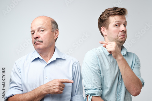 Portrait of a angry young man pointing finger at you camera gesture isolated on gray wall background