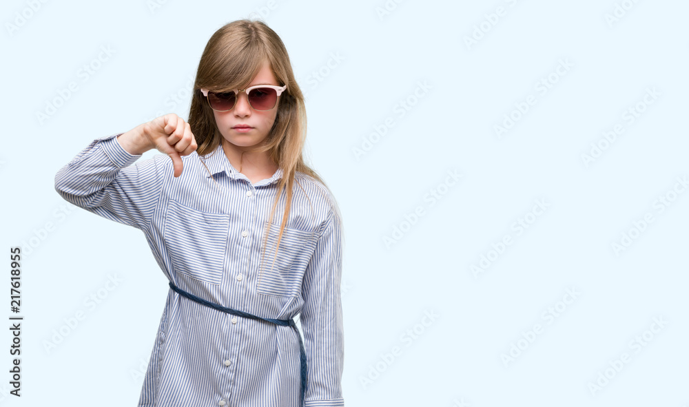 Young blonde toddler wearing blue shirt with angry face, negative sign showing dislike with thumbs down, rejection concept Young blonde toddler wearing blue shirt with angry face, negative sign showing dislike with thumbs down, rejection concept