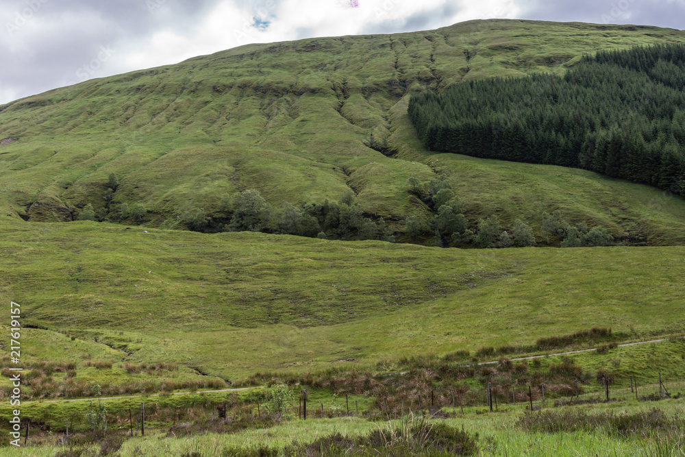 Bridge of Orchy, Scotland, UK - June 12, 2012: Green hills with pasture and forests descend towards Loch Tulla. Rural road at bottom barely visible.