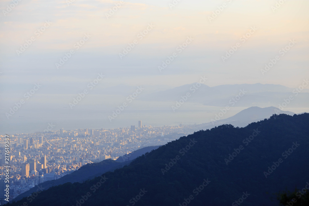Late afternoon sun hits sprawling downtown Kobe on the edge of forested hills at the base of Mt. Rokko