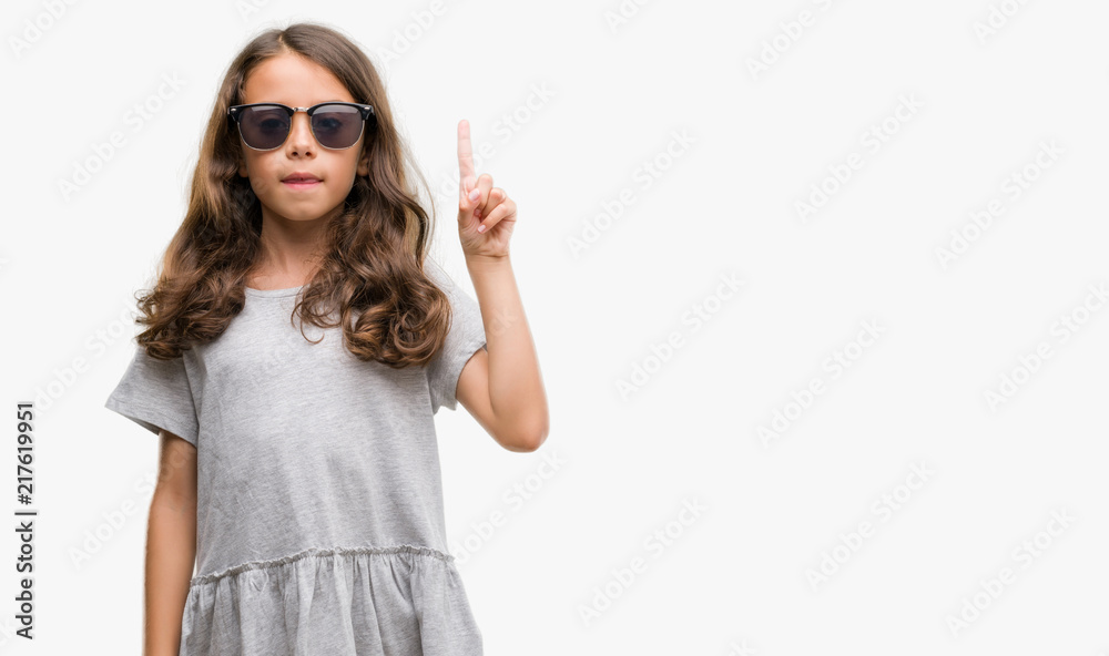 Brunette hispanic girl wearing sunglasses showing and pointing up with finger number one while smiling confident and happy. Brunette hispanic girl wearing sunglasses showing and pointing up with finger number one while smiling confident and happy.