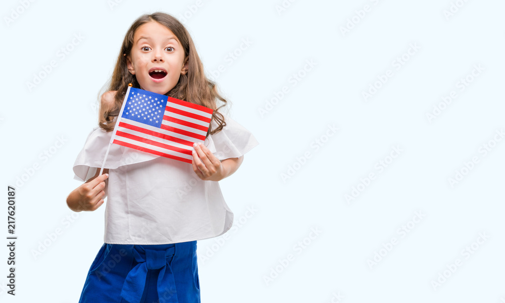 Brunette hispanic girl holding flag of United States of America scared in shock with a surprise face, afraid and excited with fear expression Brunette hispanic girl holding flag of United States of America scared in shock with a surprise face, afraid and excited with fear expression