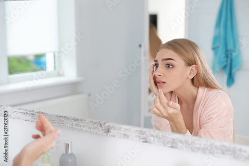 Young woman with eyelash loss problem looking in mirror indoors