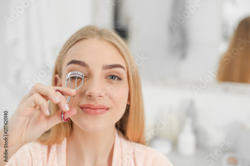 Attractive young woman curling her eyelashes indoors