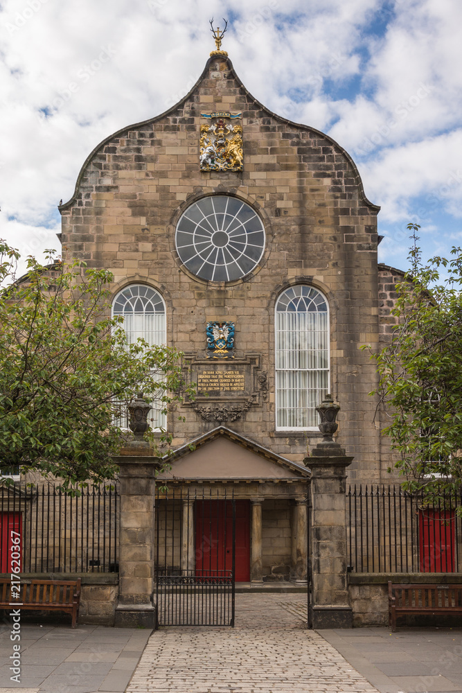 Edinburgh, Scotland, UK - June 12, 2012: Brown stone Canongate Kirk entrance and front facade under cloudy blue sky. Green foliage on the sides.