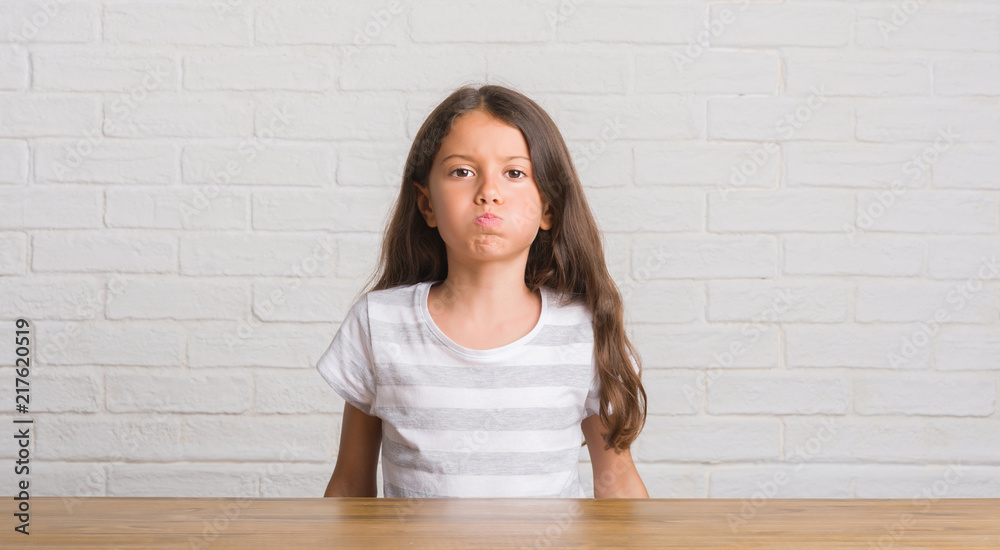 Young hispanic kid sitting on the table at home puffing cheeks with funny face. Mouth inflated with air, crazy expression. Young hispanic kid sitting on the table at home puffing cheeks with funny face. Mouth inflated with air, crazy expression.
