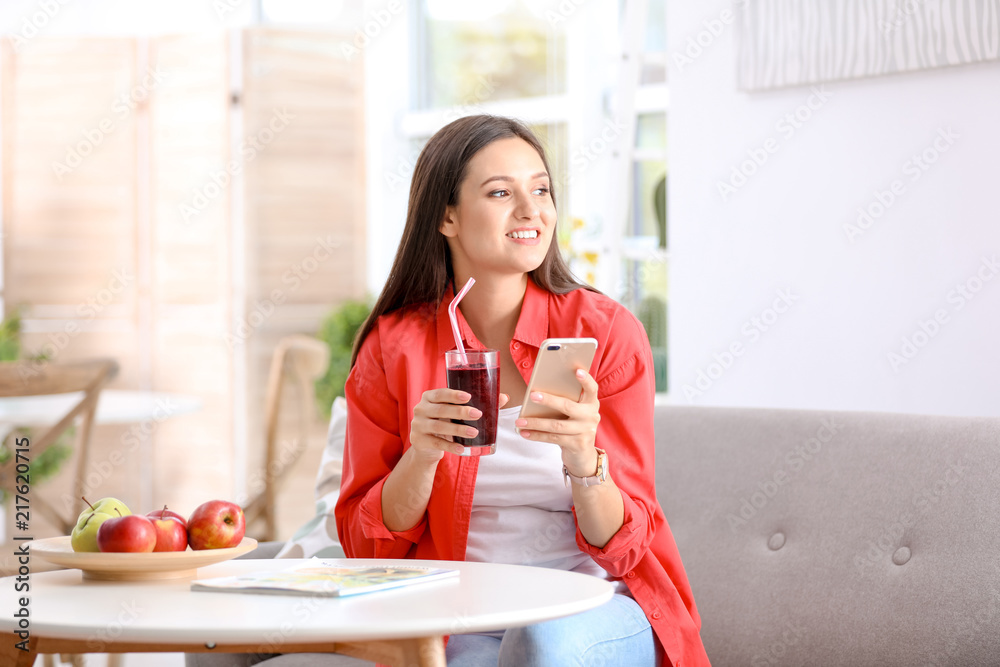 Young woman using mobile phone while drinking tasty healthy smoothie at table, indoors Young woman using mobile phone while drinking tasty healthy smoothie at table, indoors