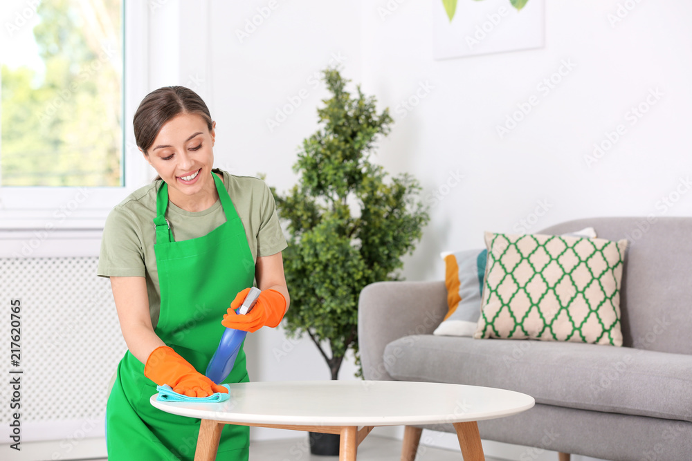 Young woman cleaning table with rag indoors
