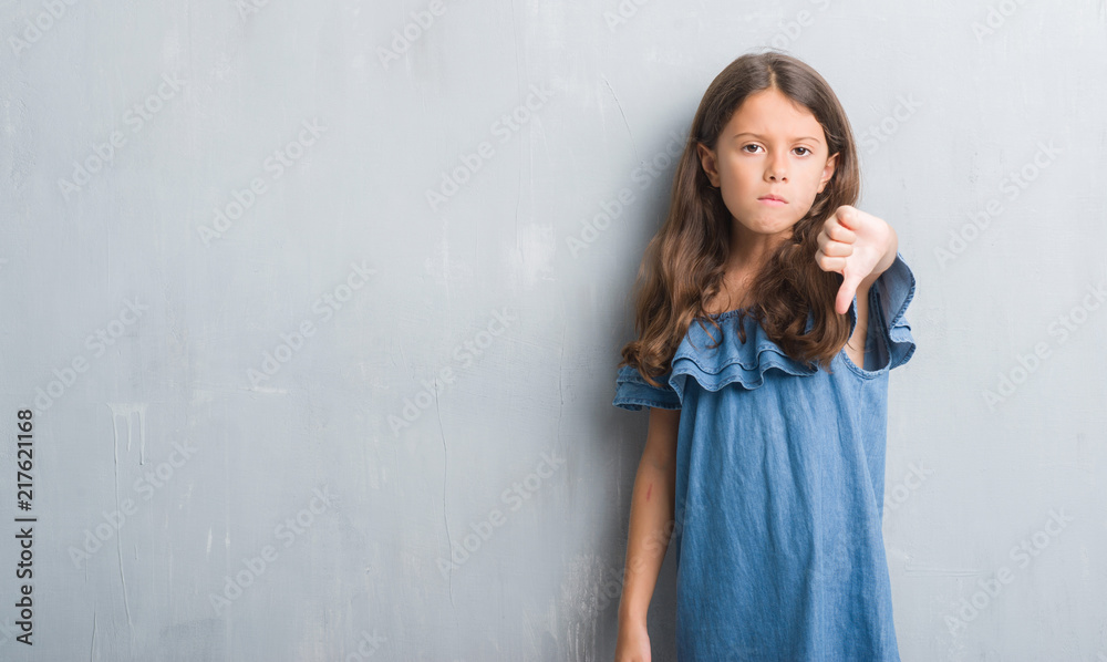 Fototapeta premium Young hispanic kid over grunge grey wall looking unhappy and angry showing rejection and negative with thumbs down gesture. Bad expression.