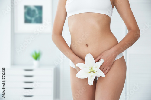 Young woman with flower showing smooth skin after bikini epilation indoors