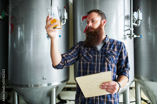 brewer checking beer for qaulity at brewery while holding clipboard photo
