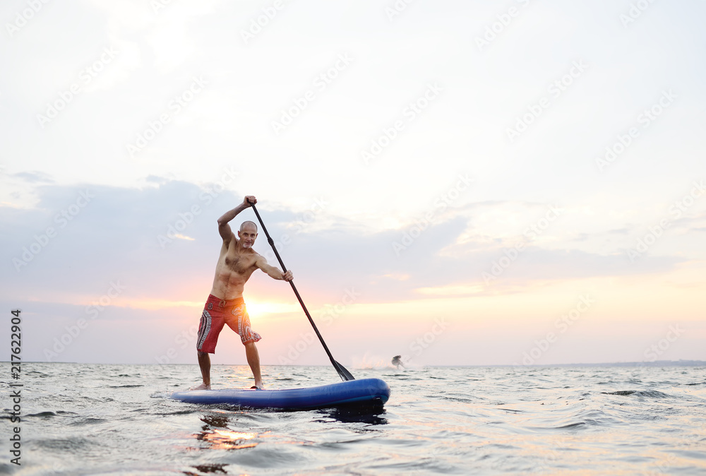 Naklejka premium A man stands on a SUP board against the background of the sea and the sunset.